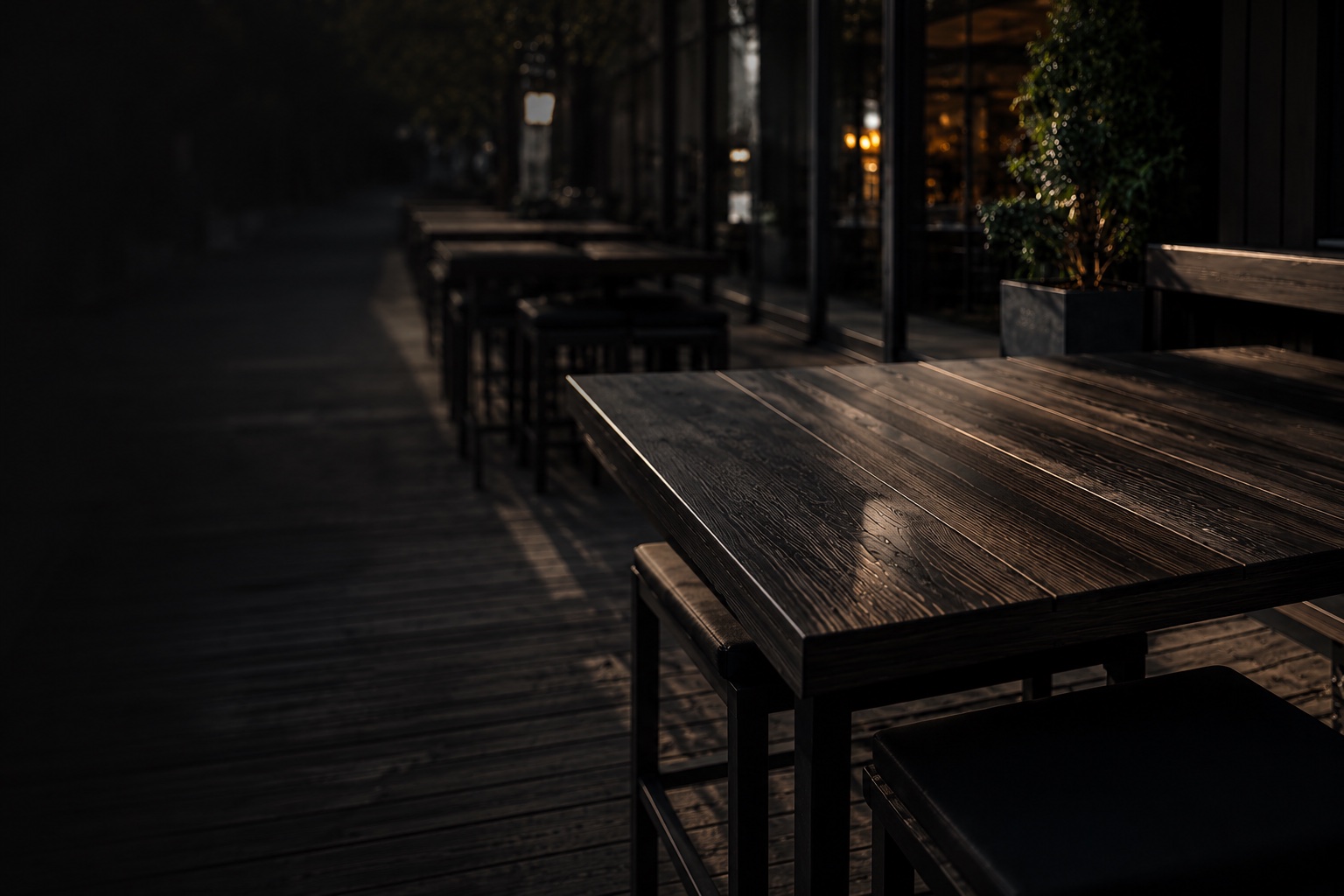 Abendstimmung auf einer eingefassten Gastro-Terrasse — dunkles Holz, Pflanzkübel, warm beleuchtete Fenster